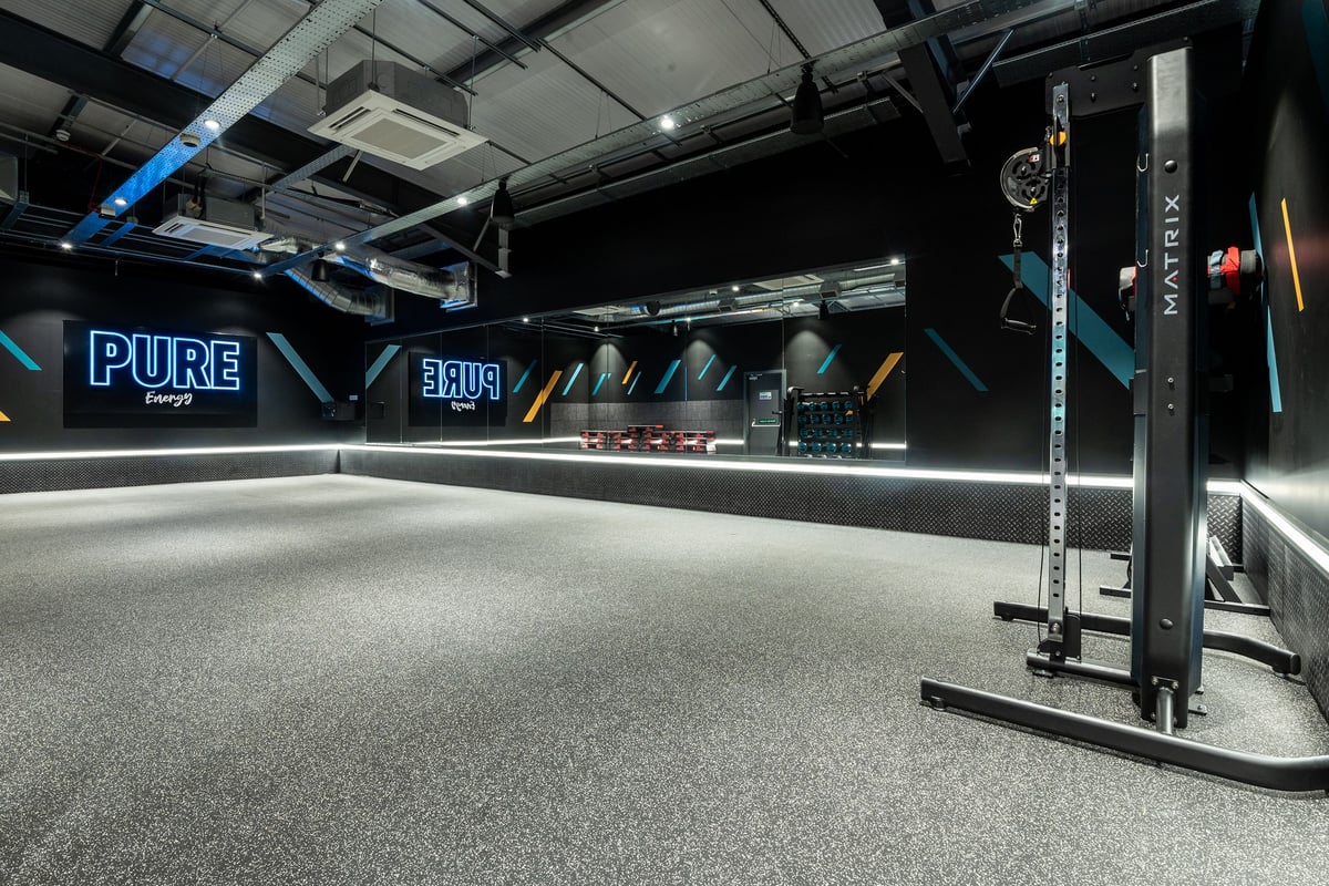 PureGym Glasgow Rutherglen: Weightlifting power racks, rig, rubberized turf floor, neon signage in dark studio.