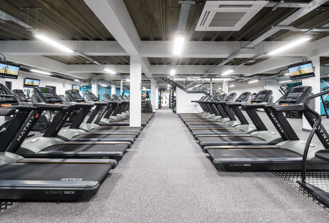 PureGym Brighton London Road: Rows of treadmills bathed in bright light under a ceiling of exposed beams.