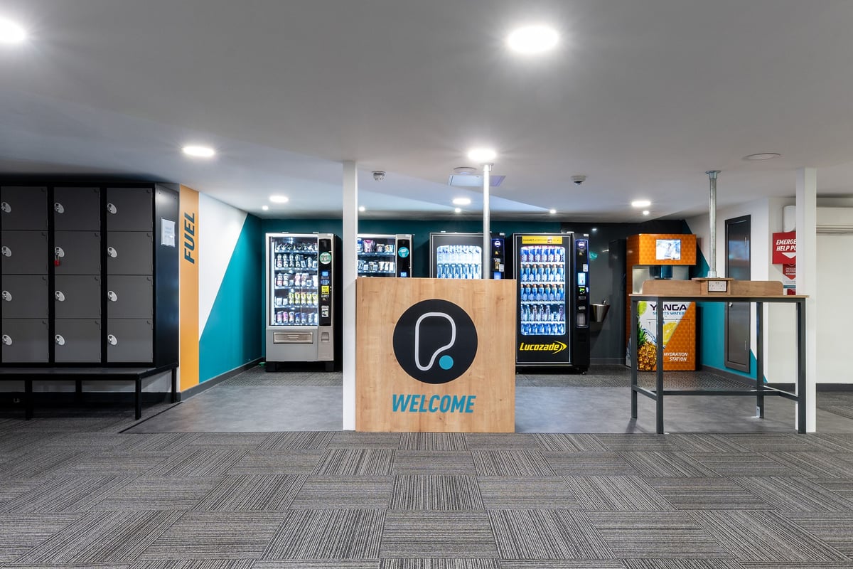 PureGym Lincoln St Marks Centre: Vending machines, lockers, and a welcome sign in an amenity area.