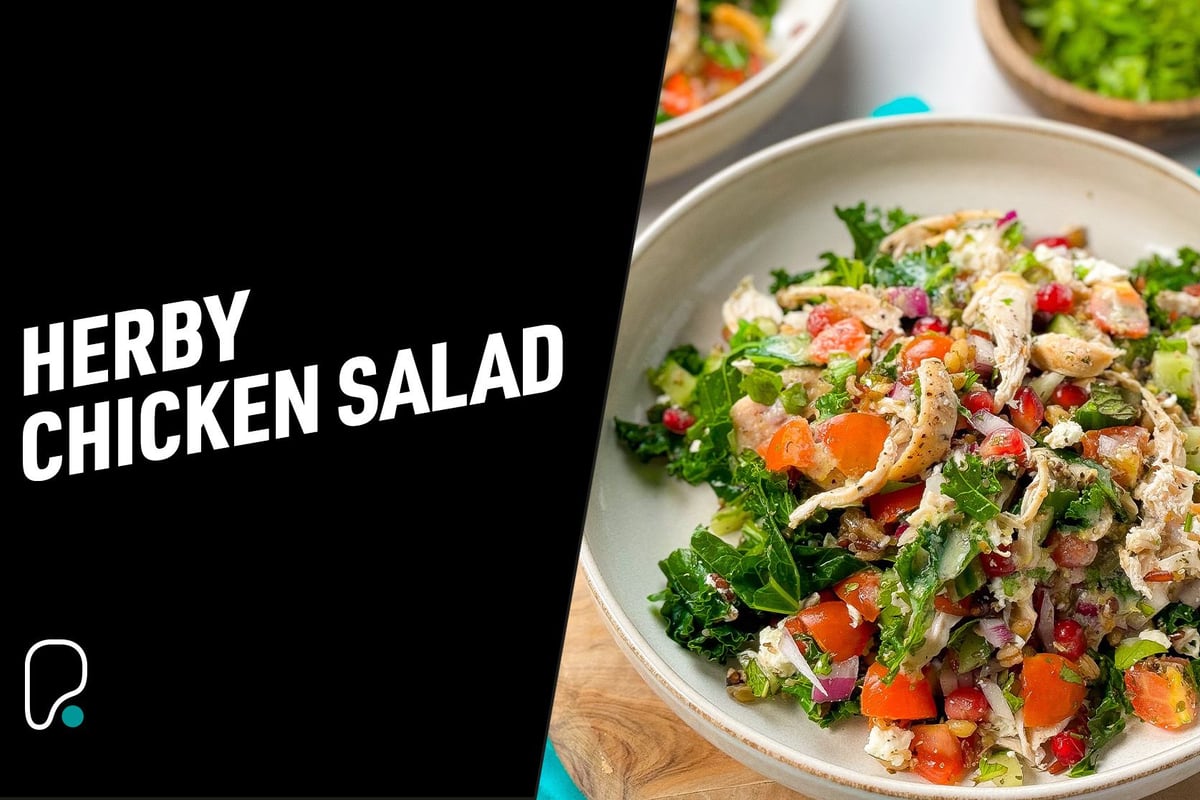 Bowl of herby chicken salad with kale, tomatoes, pomegranate seeds, and onions.