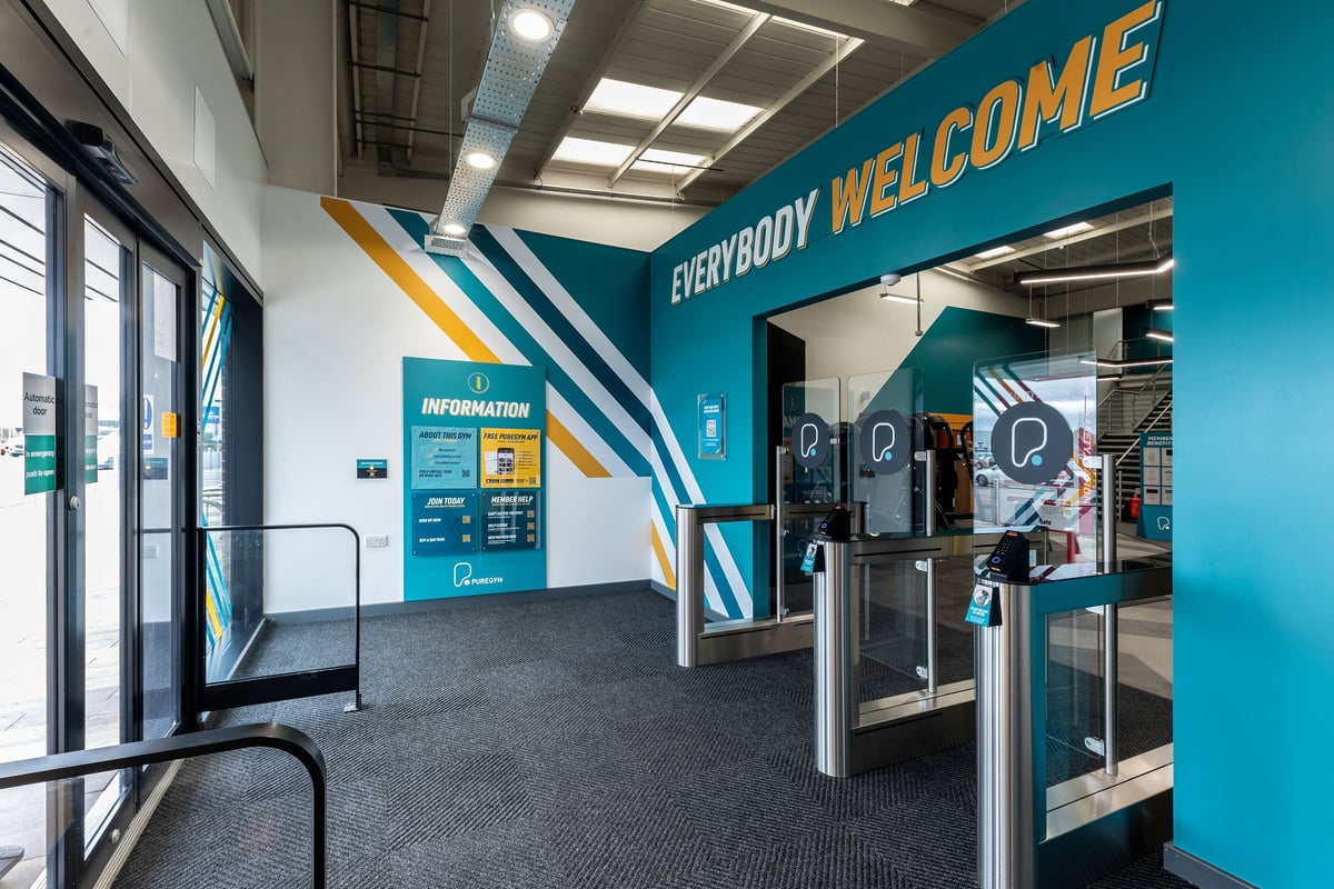 PureGym Eastbourne: Entrance area with speed gates, everybody welcome wall art, and an informational display.