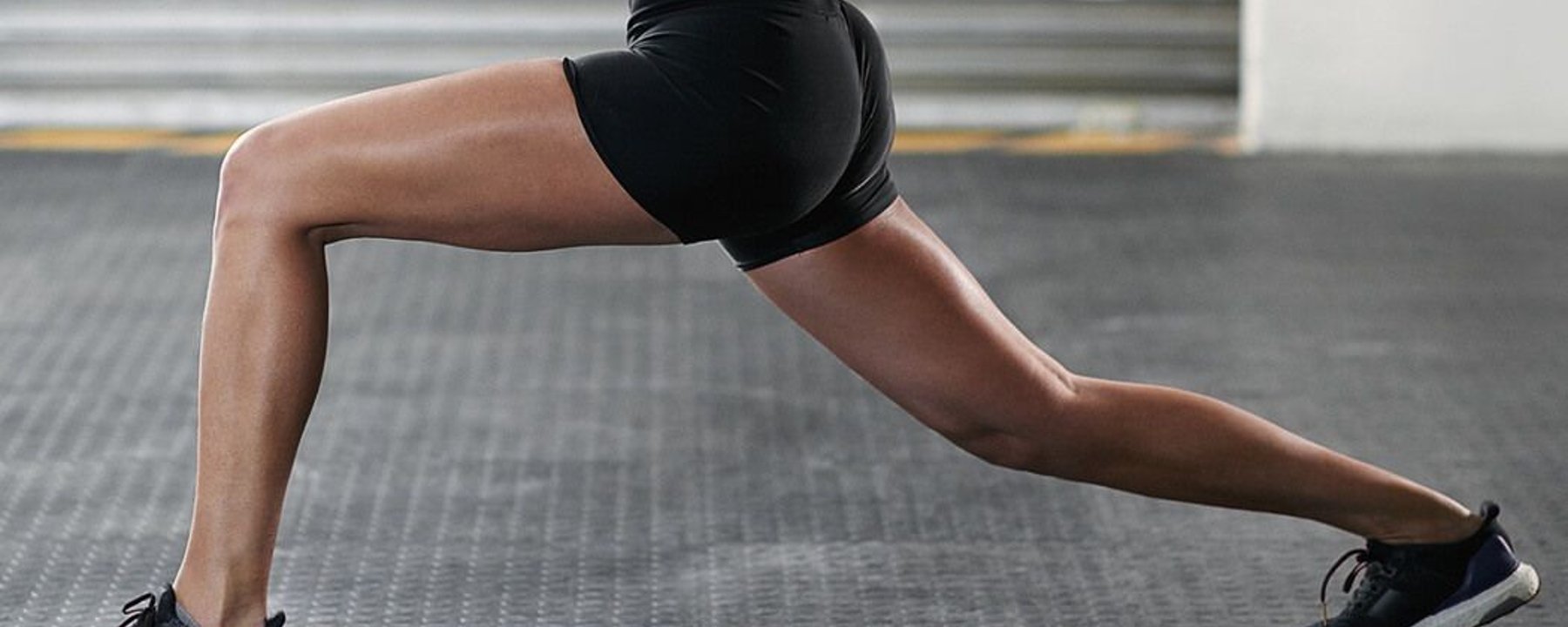 Person in black shorts and trainers performing a lunge on a gym floor