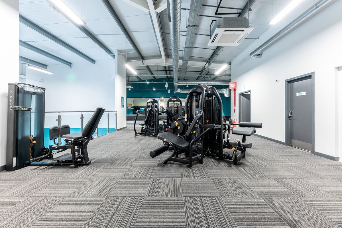 PureGym Galashiels: Strength training area with weight machines, benches, and rubberized flooring.
