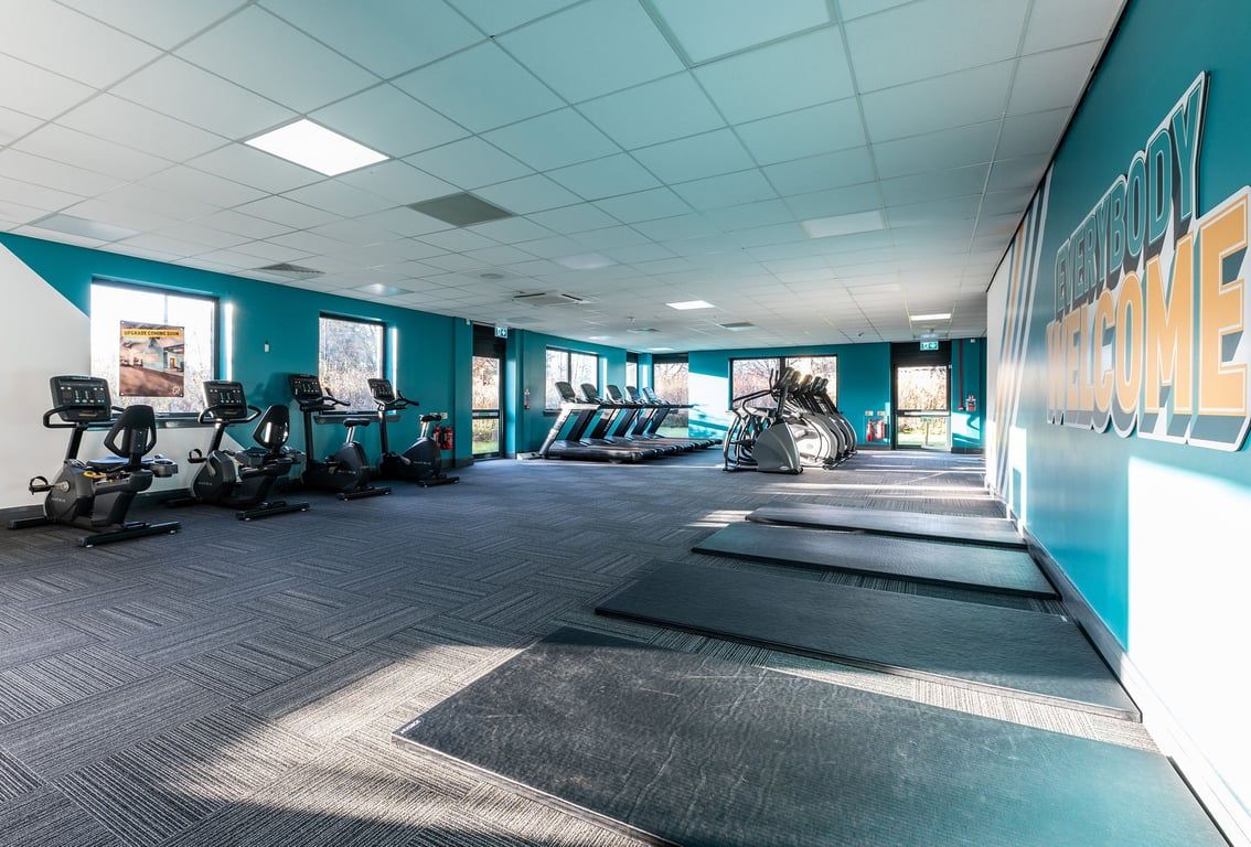 PureGym Livingston: Rows of treadmills, weight machines, exercise bikes in a teal-coloured fitness studio.