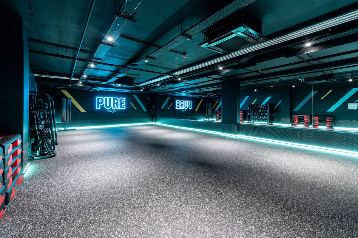 PureGym London Angel: Futuristic fitness studio with neon Pure logo, rubberized floor, and branded equipment along walls.