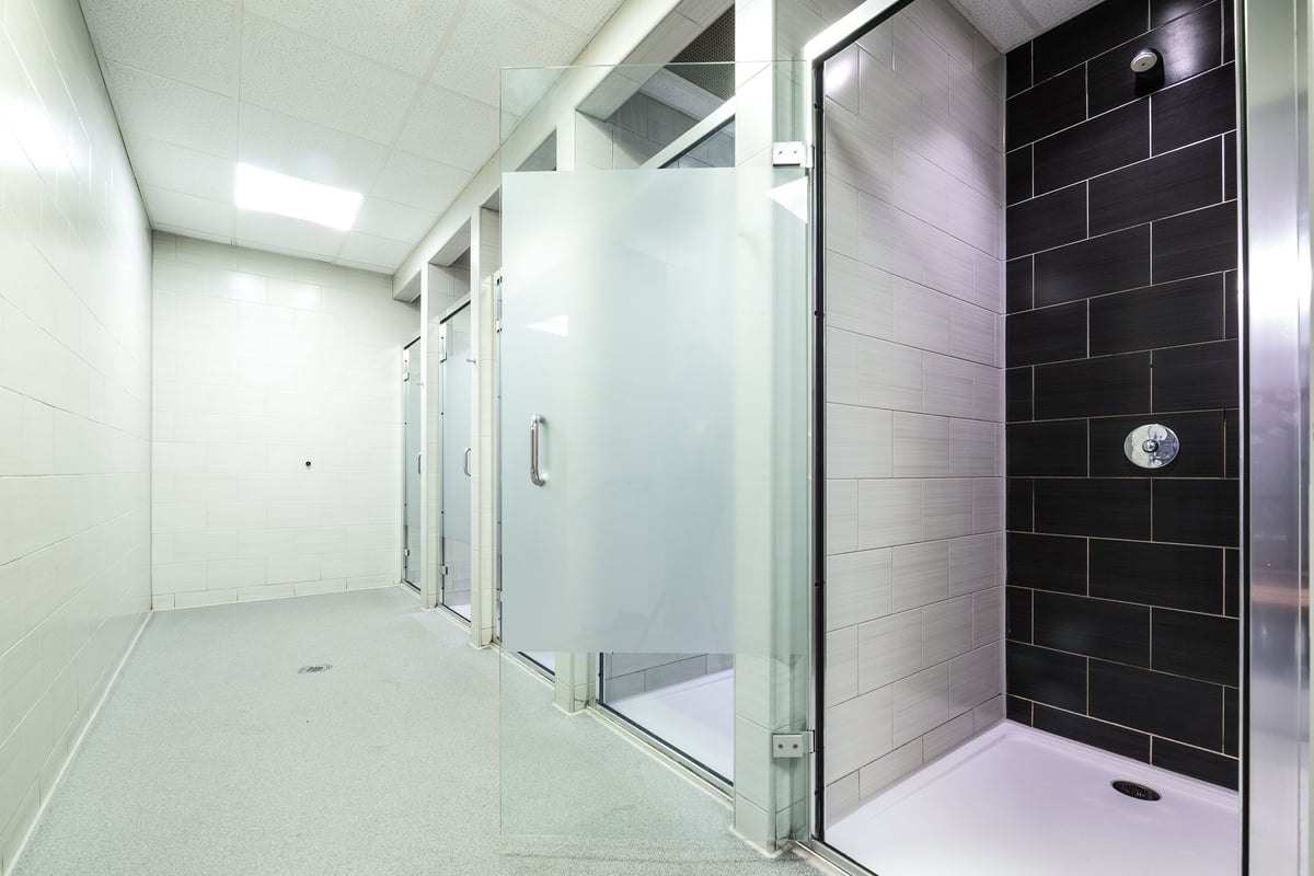PureGym Leeds Bramley: Shower and changing area with tiled walls, glass partitions, and private cubicles.