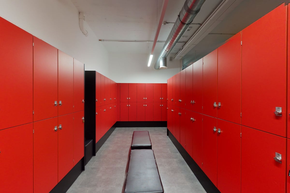 PureGym Bern Bümpliz: Des casiers et des bancs rouges dans un couloir étroit, probablement dans un gymnase ou un vestiaire.