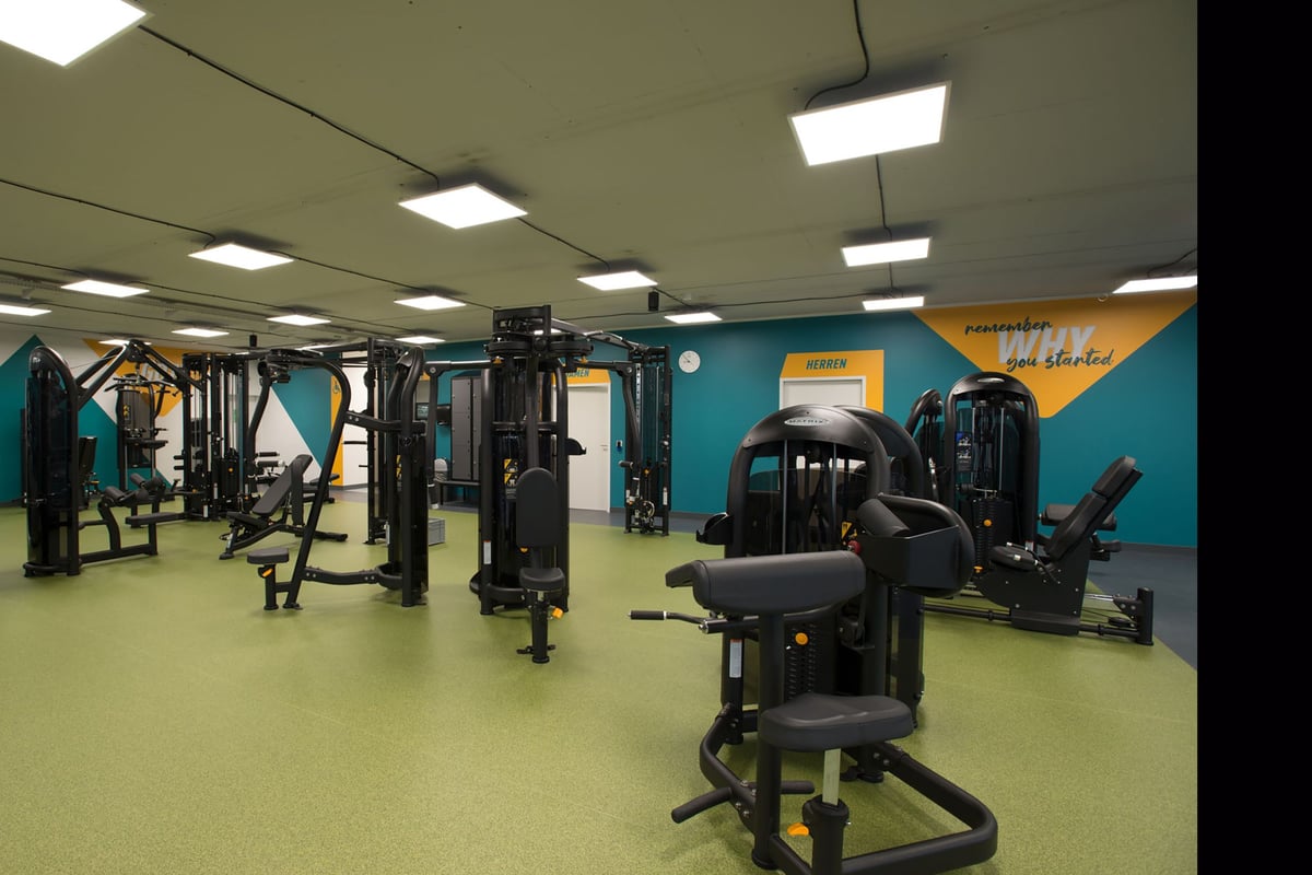 PureGym Lyss: Intérieur de la salle de sport avec appareils de musculation, stations de téléphérique, bancs et murs décoratifs de couleur sarcelle.