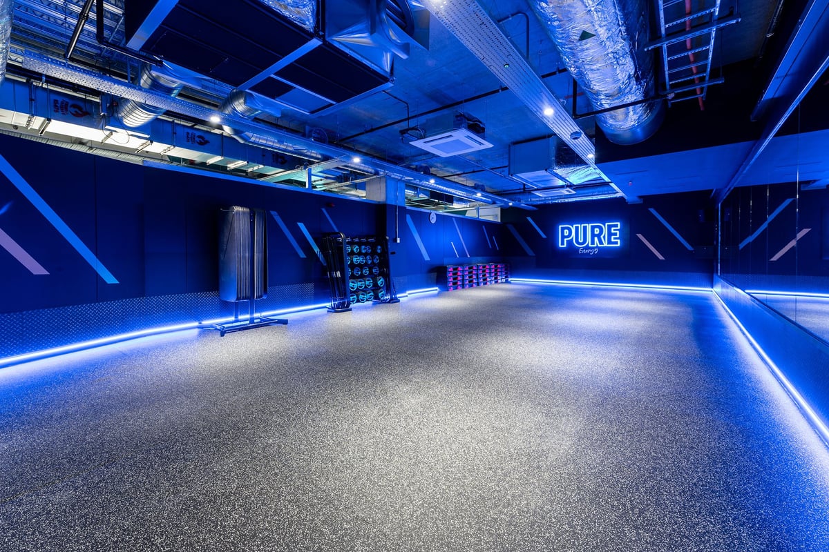 PureGym London Hoxton: Rubberized blue flooring, exposed ceiling ducts, dimmed lighting, and 'PURE' signage.