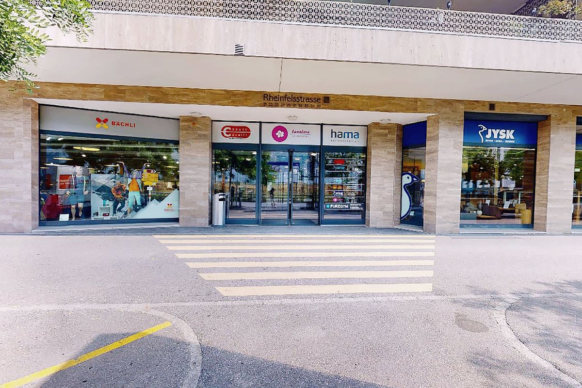 PureGym Chur: Ladenfronten, Fussgängerüberweg und ein paar Leute vor einem Einzelhandelsviertel mit mehreren Ladenfronten.