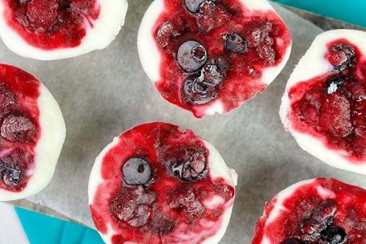 Frozen yoghurt cups with mixed berries on parchment and turquoise cloth
