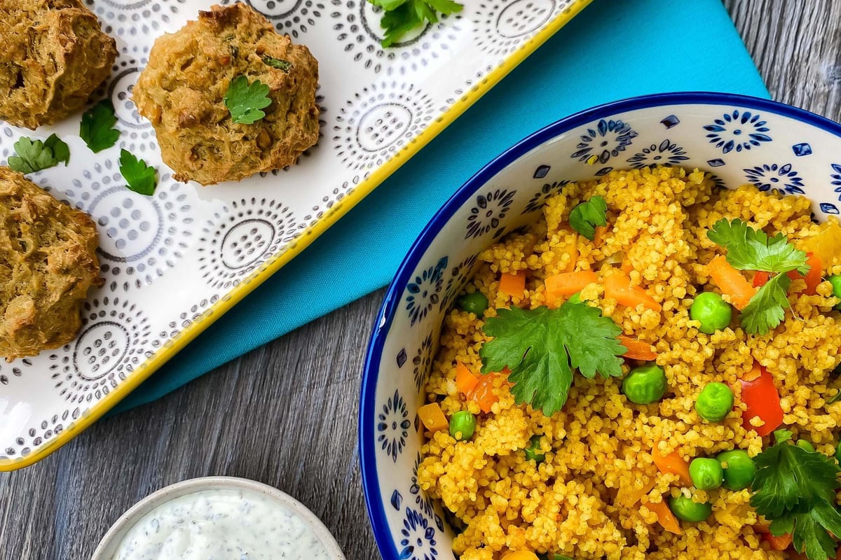 Falafel balls on a patterned tray with couscous salad and yoghurt dip on a wooden table