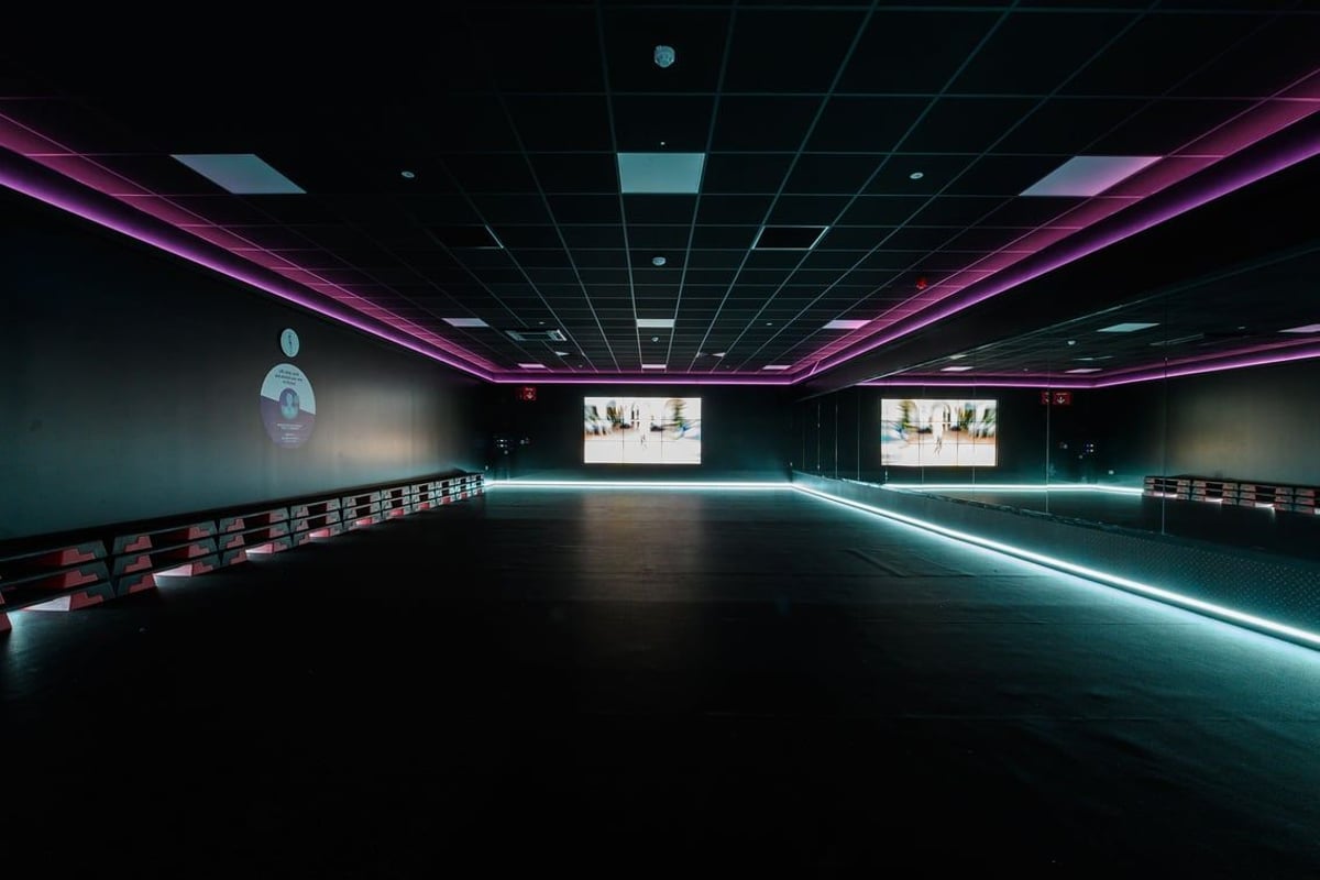 PureGym Salisbury: Mirrored studio with purple lighting and rows of empty benches.