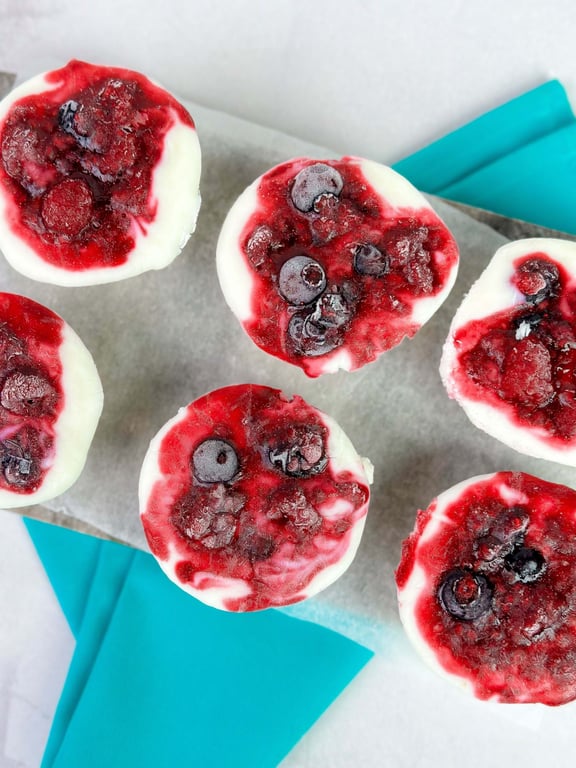 Frozen yoghurt cups topped with mixed berries on parchment and blue napkins