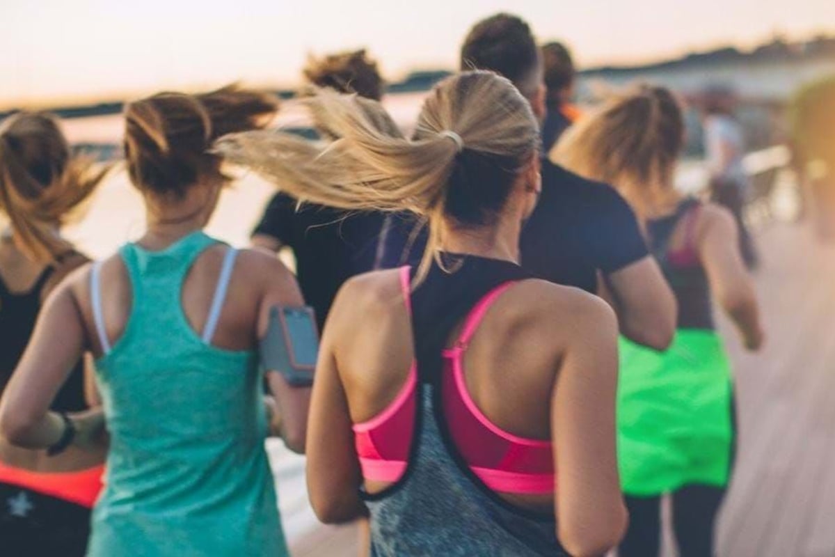 Group of people running outdoors near water at sunset wearing sportswear.