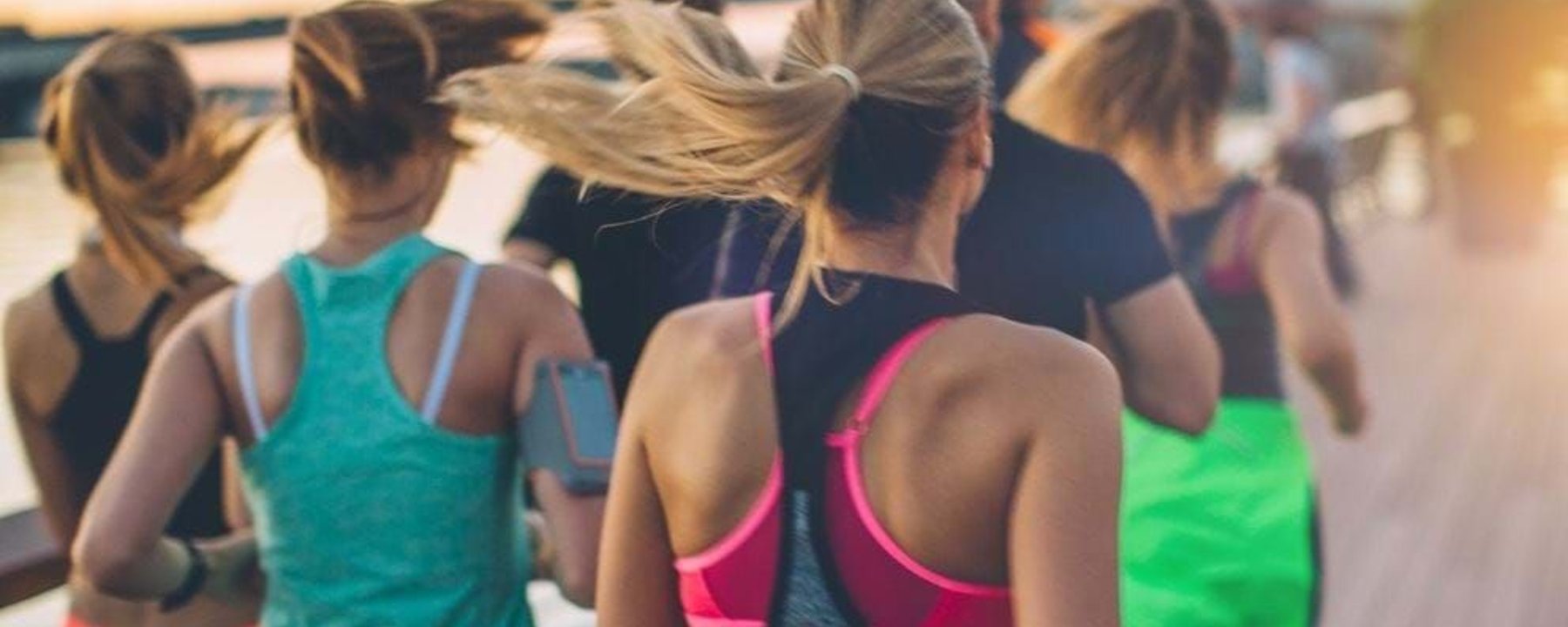 Group of people running outdoors near water at sunset wearing sportswear.