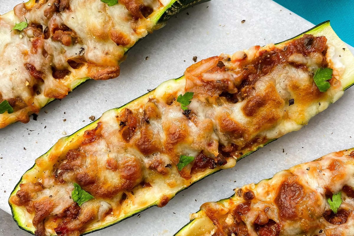 Three baked zucchini halves topped with melted cheese, minced meat, and parsley on a white