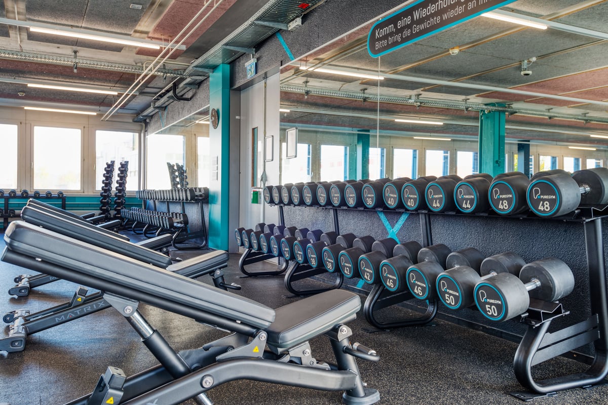 PureGym Wetzikon: Freigewichte und Bänke an einer Spiegelwand.