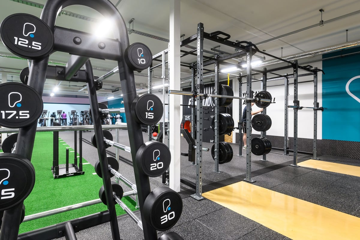 PureGym Bristol Abbey Wood Retail Park: Weightlifting area with squat racks, free weights, turf flooring, and mirrored walls.