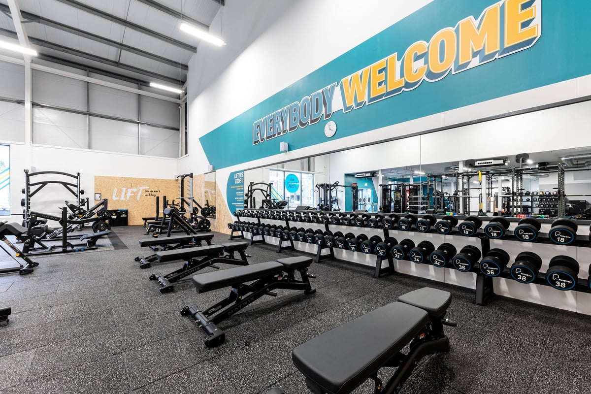 PureGym Galashiels: Weight benches, dumbbell racks, free weights, and a teal "Welcome" sign in a gym setting.