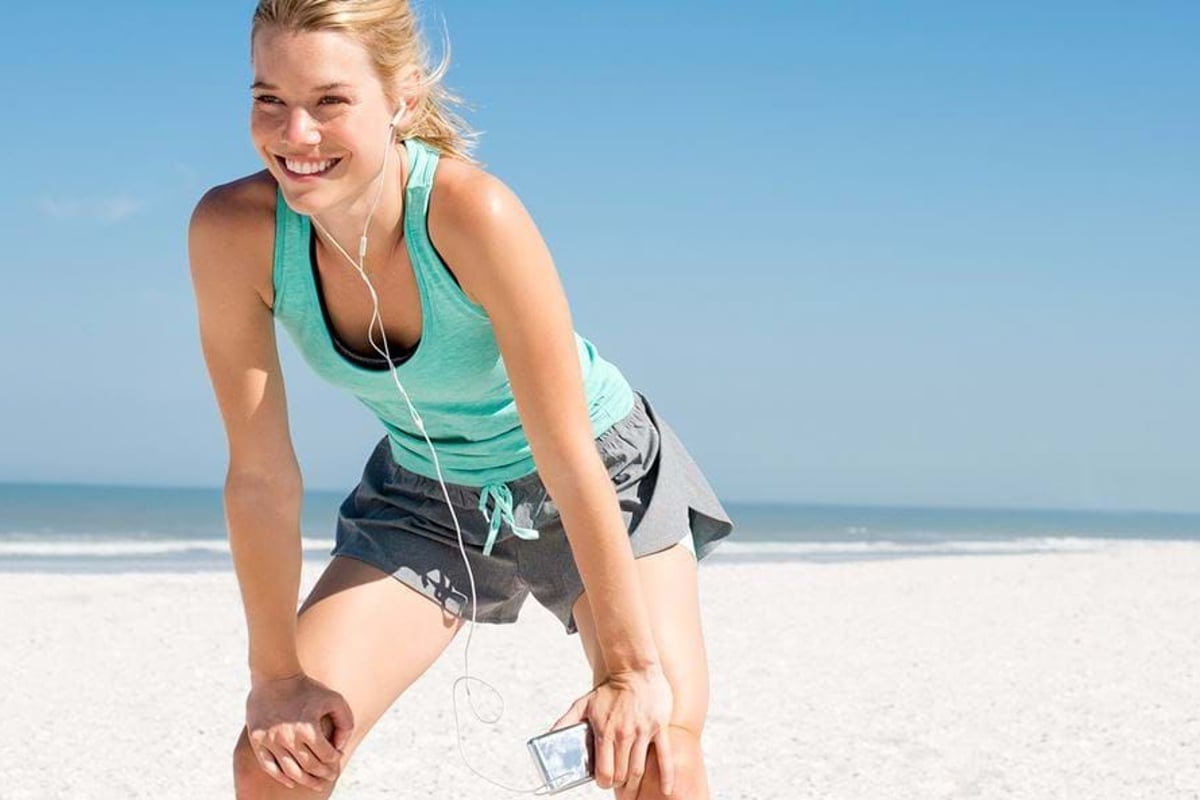 Smiling woman in sportswear listening to music and resting on a sandy beach