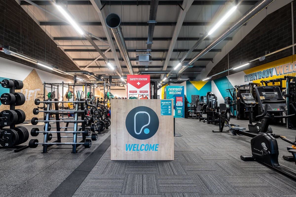 PureGym Aberdare: Free weights, weight plates, squat racks, machines, welcome sign, and rubberized flooring in a gym setting.