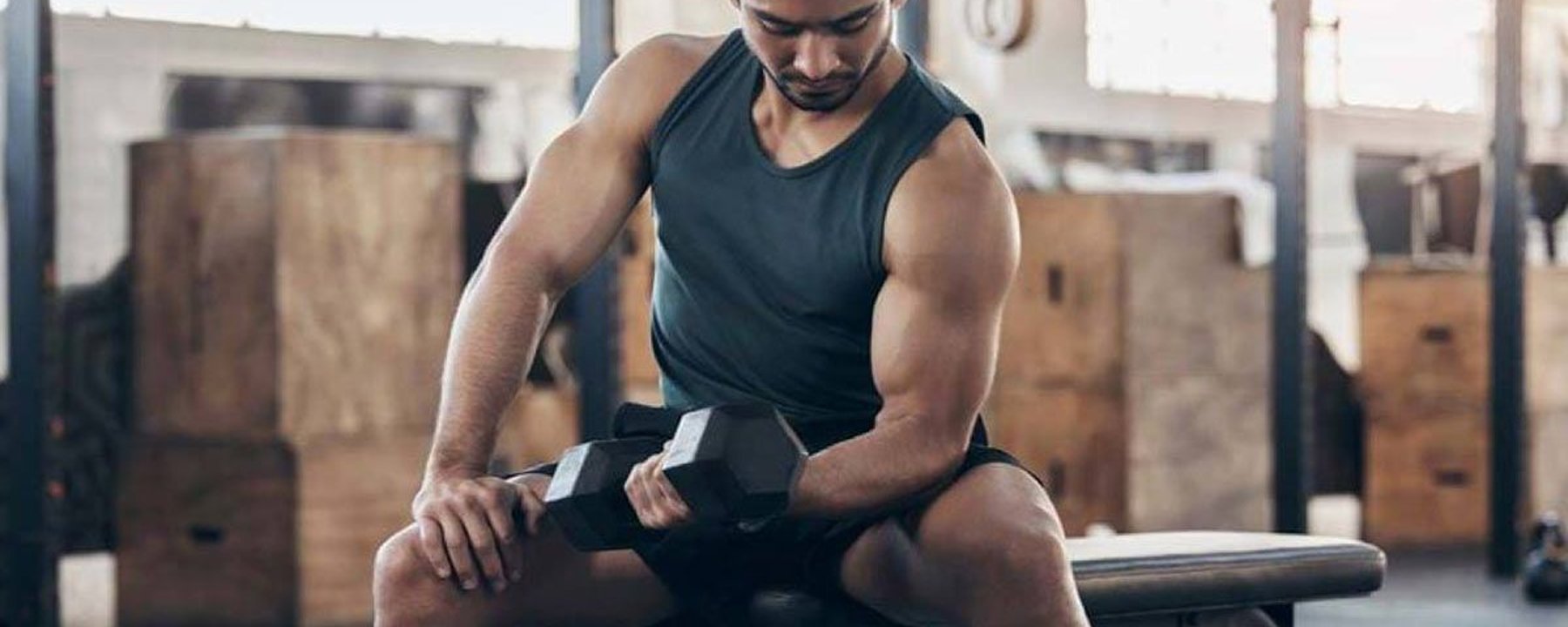 Man in black tank top lifting dumbbell while sitting on gym bench