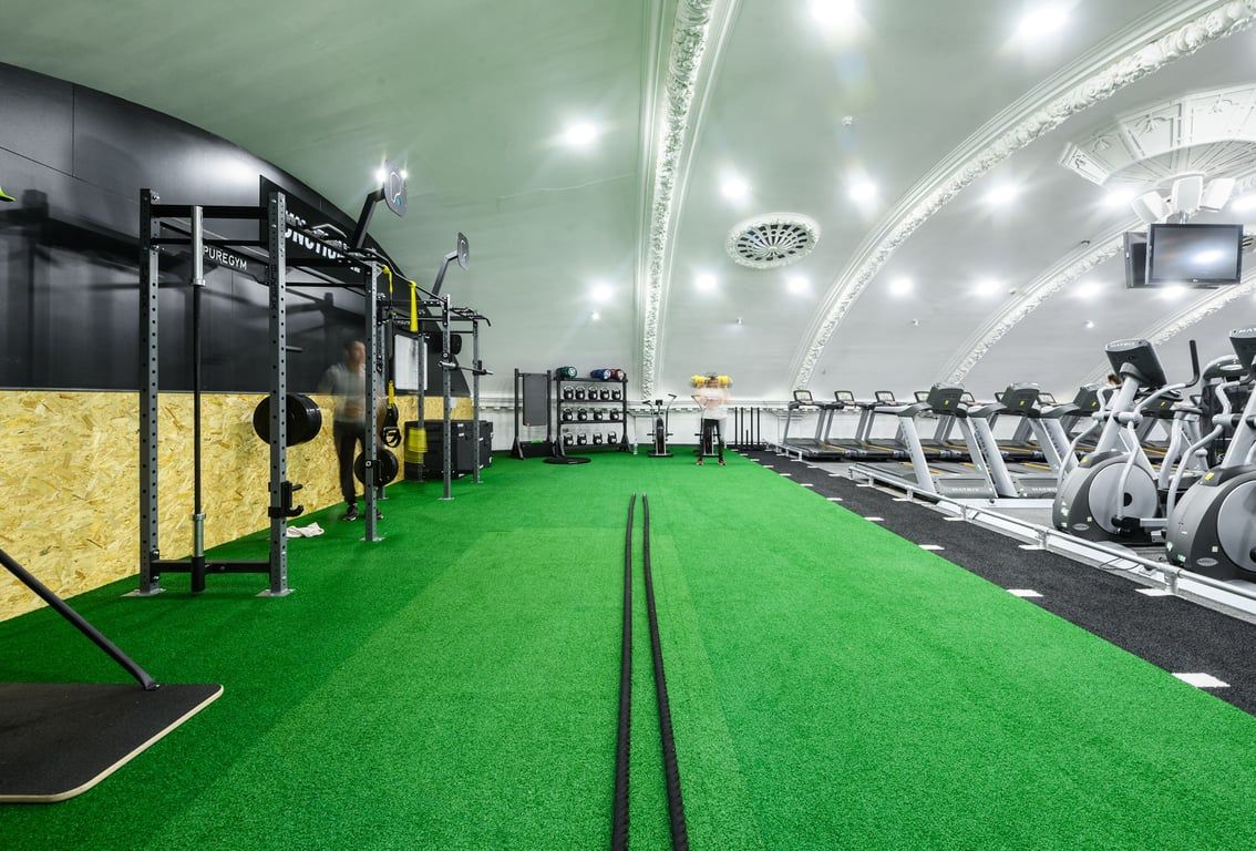PureGym London Wandsworth: Green turf, weight racks, resistance bands, slam balls, and cardio machines in a gym setting.