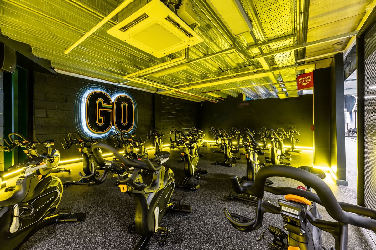 PureGym Newcastle Eldon Garden: Rows of stationary bikes bathed in neon yellow lighting in an indoor cycling studio.