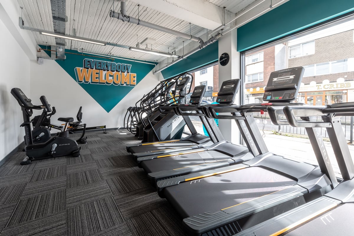 PureGym London Hornchurch: Rows of treadmills and stationary bikes with a welcome banner in a well-lit gym interior.