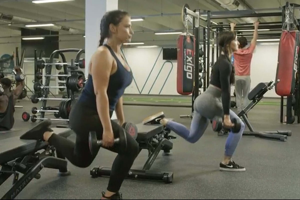 Two women doing Bulgarian split squats with dumbbells in a gym