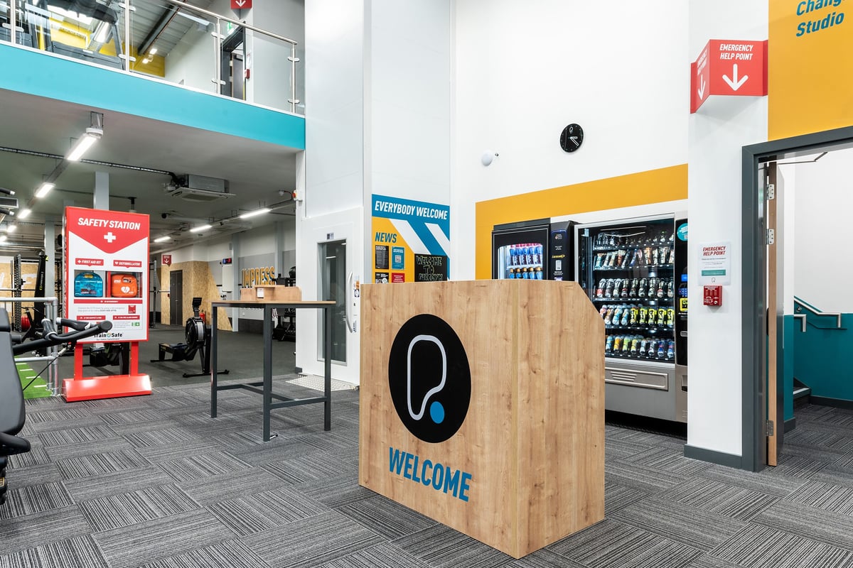 PureGym Northallerton: Welcome sign, vending machines, sales counter and directional signage in a commercial lobby.
