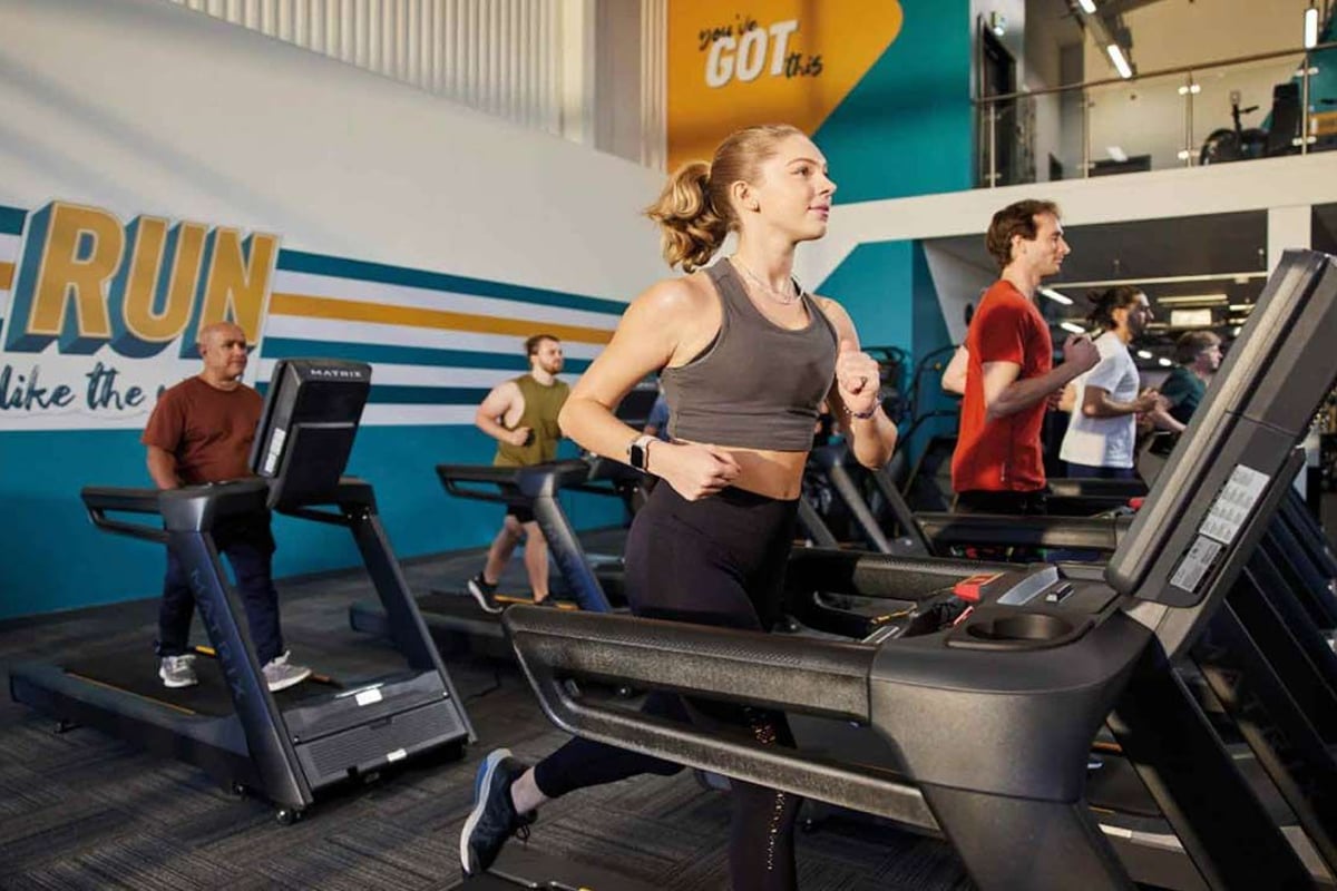 Personnes courant sur des tapis de course dans une salle avec un texte motivant au mur