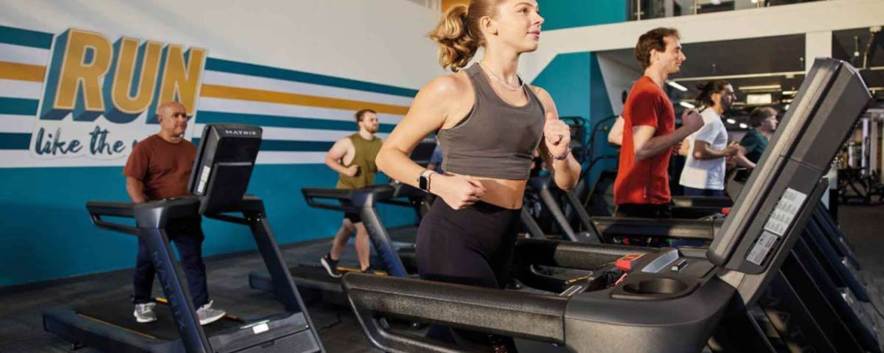 Menschen laufen auf Laufbändern im Fitnessstudio vor motivierendem Wandtext