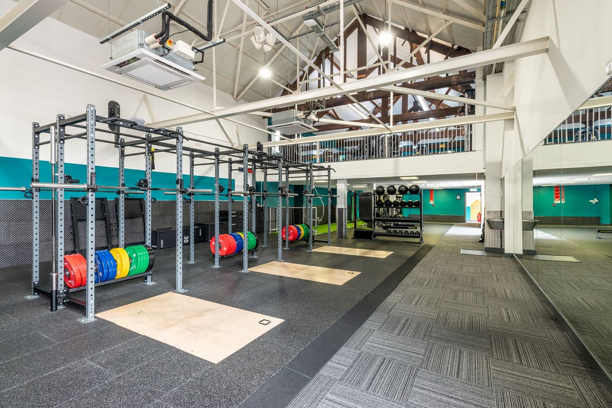 PureGym Northwich: Weightlifting racks, weight plates, rubberized flooring, and open workout area with mirrored walls.