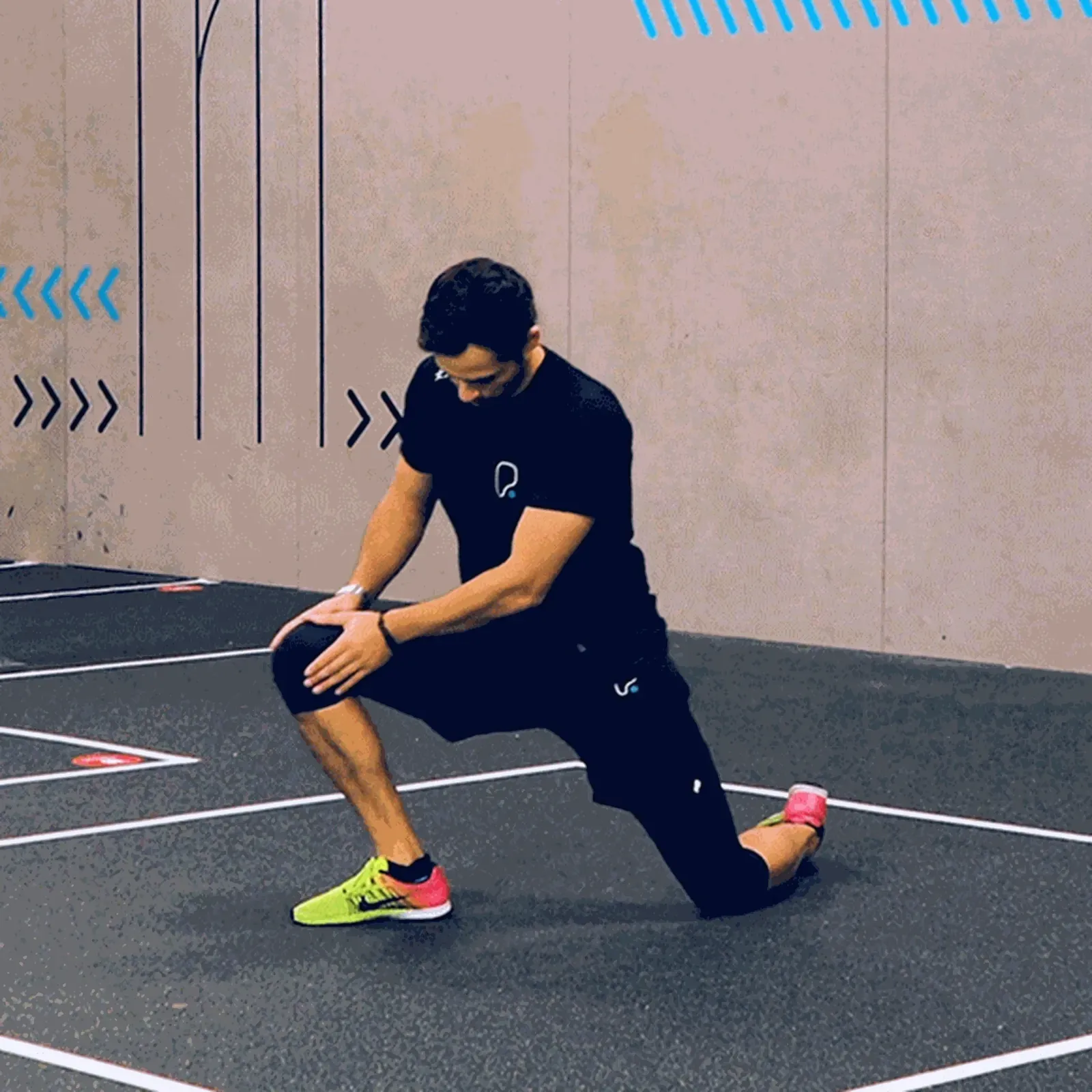 Man in black sportswear performing a kneeling lunge stretch on a gym floor