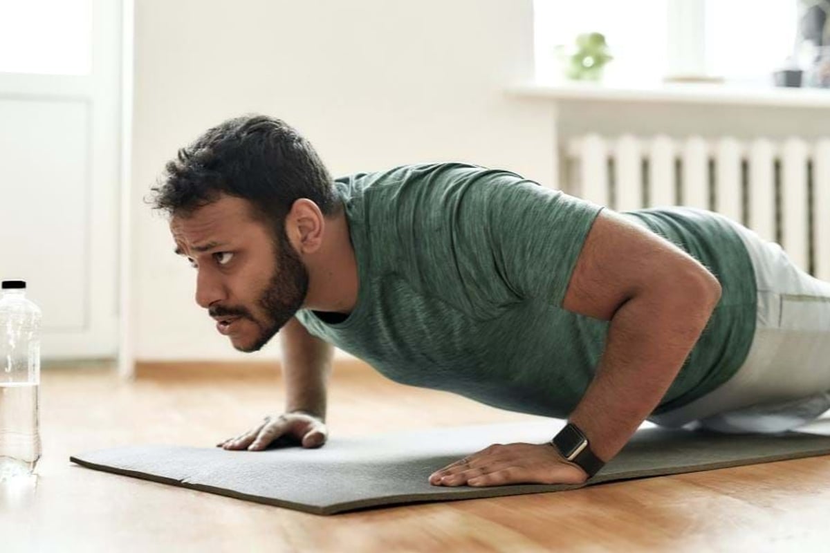 Man in green shirt doing push-ups on a mat with a water bottle nearby indoors