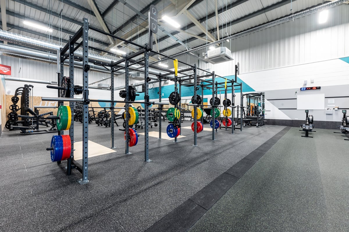 PureGym Merthyr Tydfil: Rig of squat racks, barbells, weight plates in varied hues, rubberized flooring.