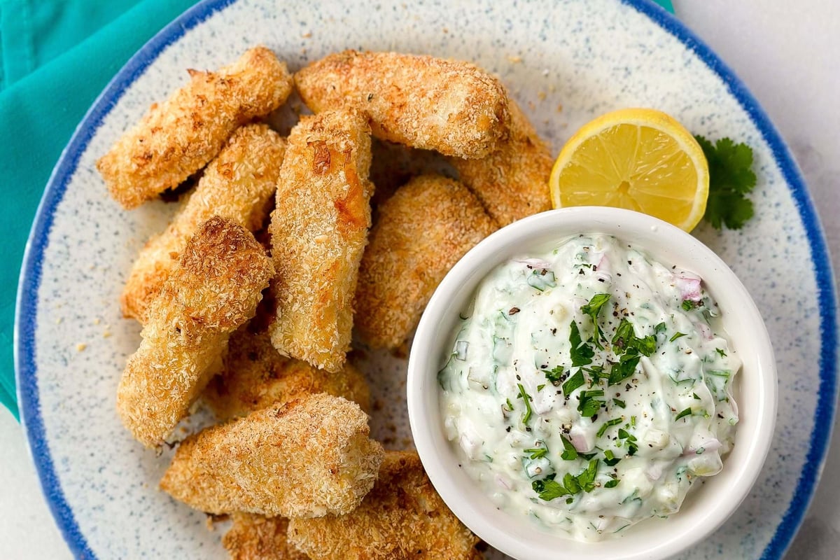 Breaded fish sticks with creamy herb dip and lemon wedge on a blue-rimmed plate