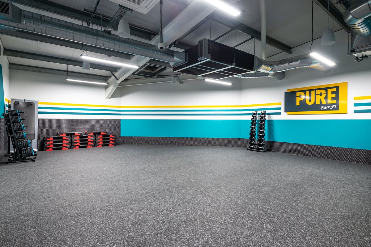 PureGym Market Harborough: Exercise studio with weight racks, colourful wall markings, ventilation ducts overhead.