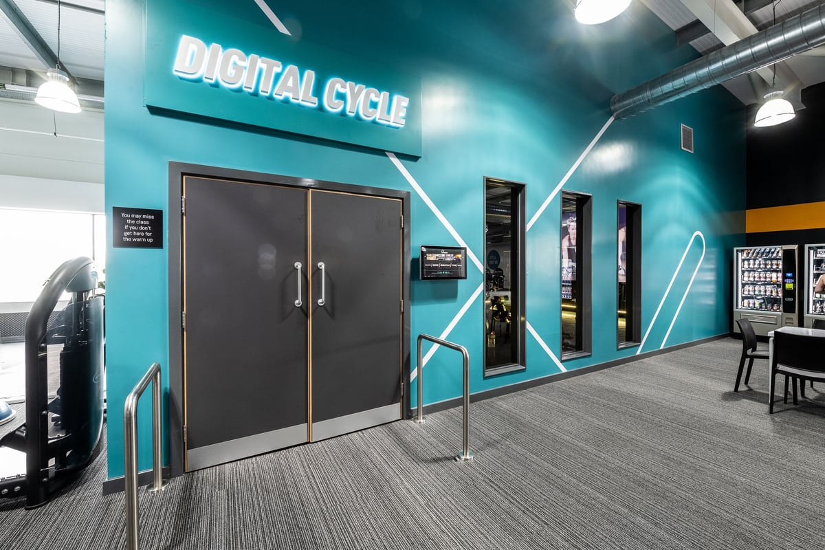 PureGym Portsmouth North Harbour: Digital cycle studio with vending machines, lockers, and branded teal accents.