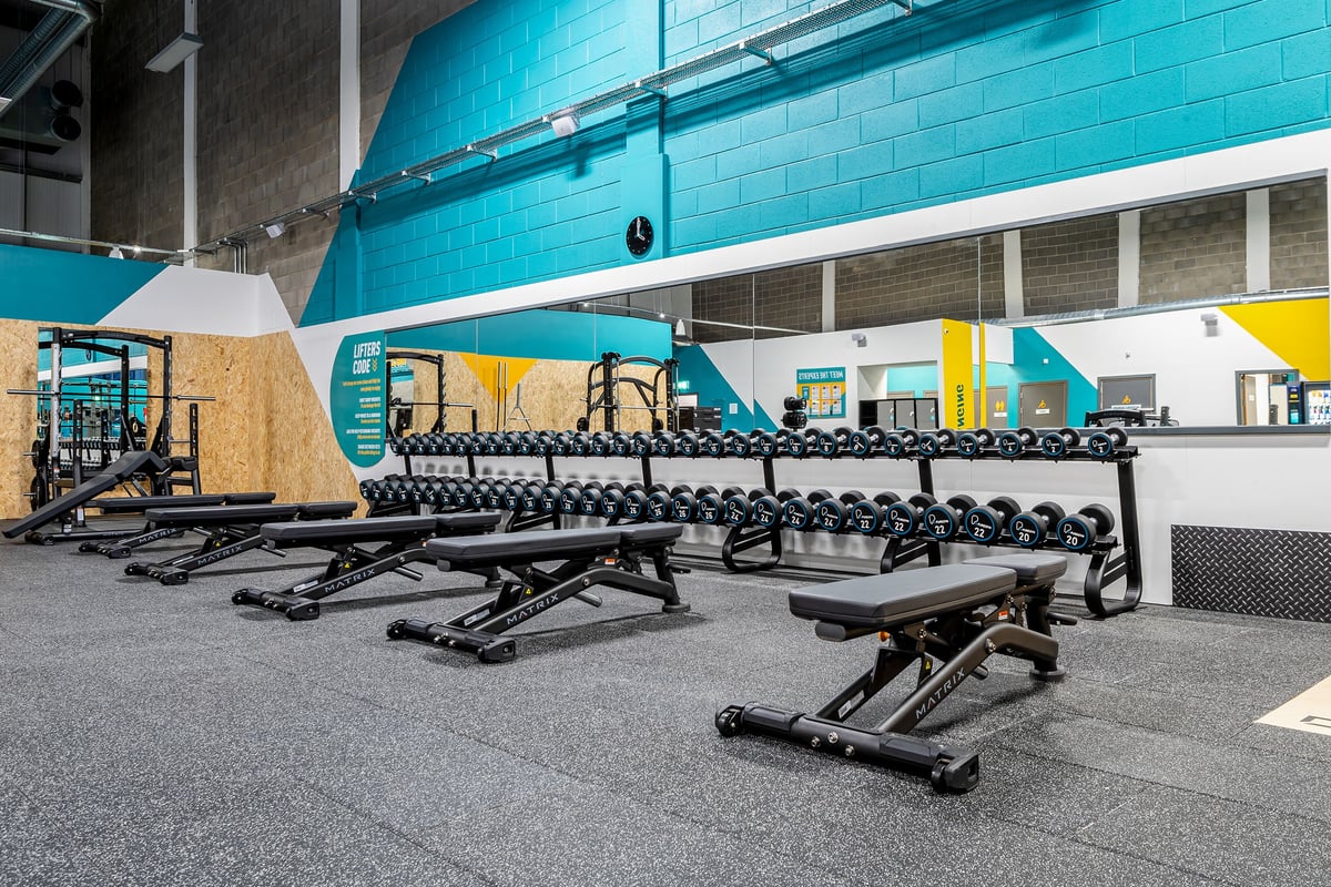 PureGym Elgin: Rows of seated weightlifting benches and racks outside a gym entrance.
