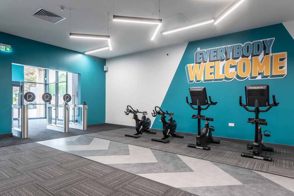 PureGym Knaesborough: Exercise bikes, turquoise walls, 'Everybody Welcome' mural, rubberised flooring.