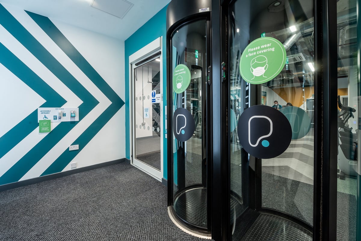 PureGym Maidstone The Mall: Glass entry doors, circular logo, teal and arrow graphics along walls indicating gym environment.