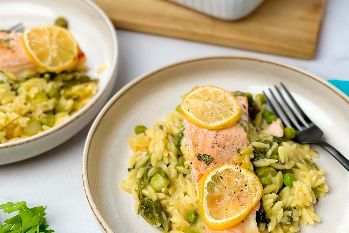 Salmon fillet with lemon slices served on orzo pasta with peas and greens
