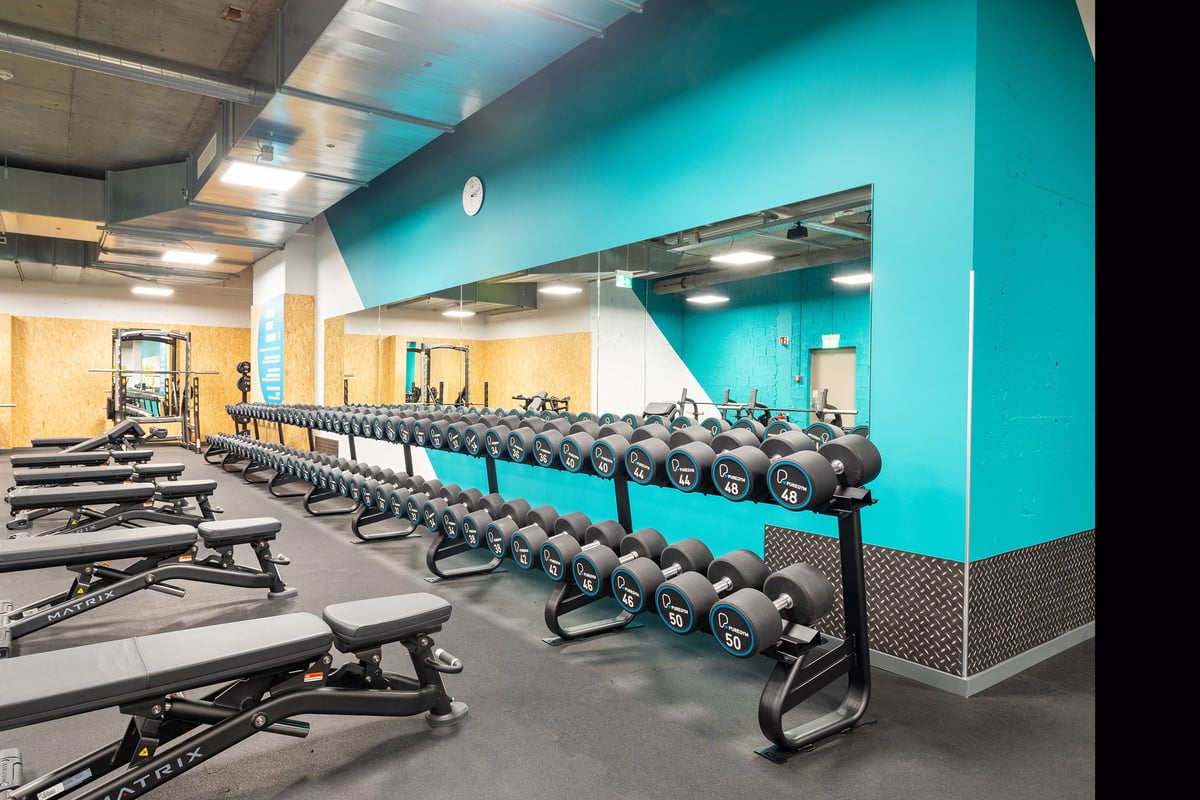 PureGym La Chaux-de-fonds: Rows of weight benches, dumbbells, and mirrored wall.