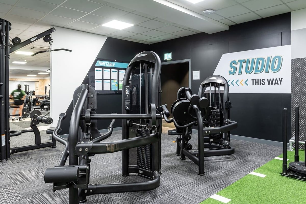 PureGym Epsom: Weight machines, exercise studio signage, black and grey colour scheme, turf floor area.