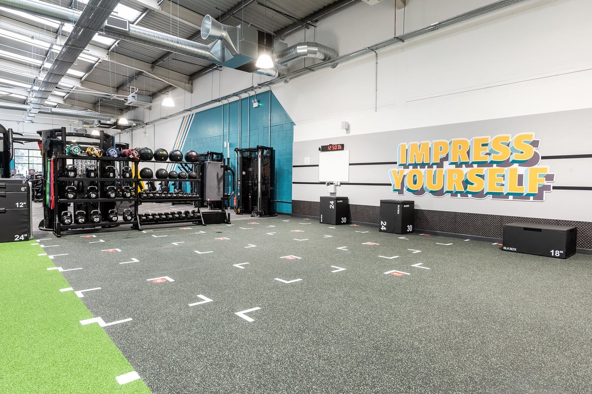 PureGym Stockport North: Weight machines, resistance bands, free weights, turf area, motivational branding on wall.