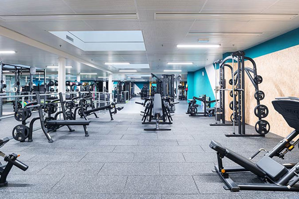 PureGym Fribourg: Salle de sport avec appareils de résistance, haltères, bancs et supports de musculation sur un sol caoutchouté.