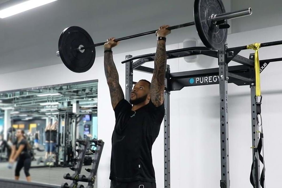 Man lifting barbell overhead in gym with mirrored wall and equipment in background